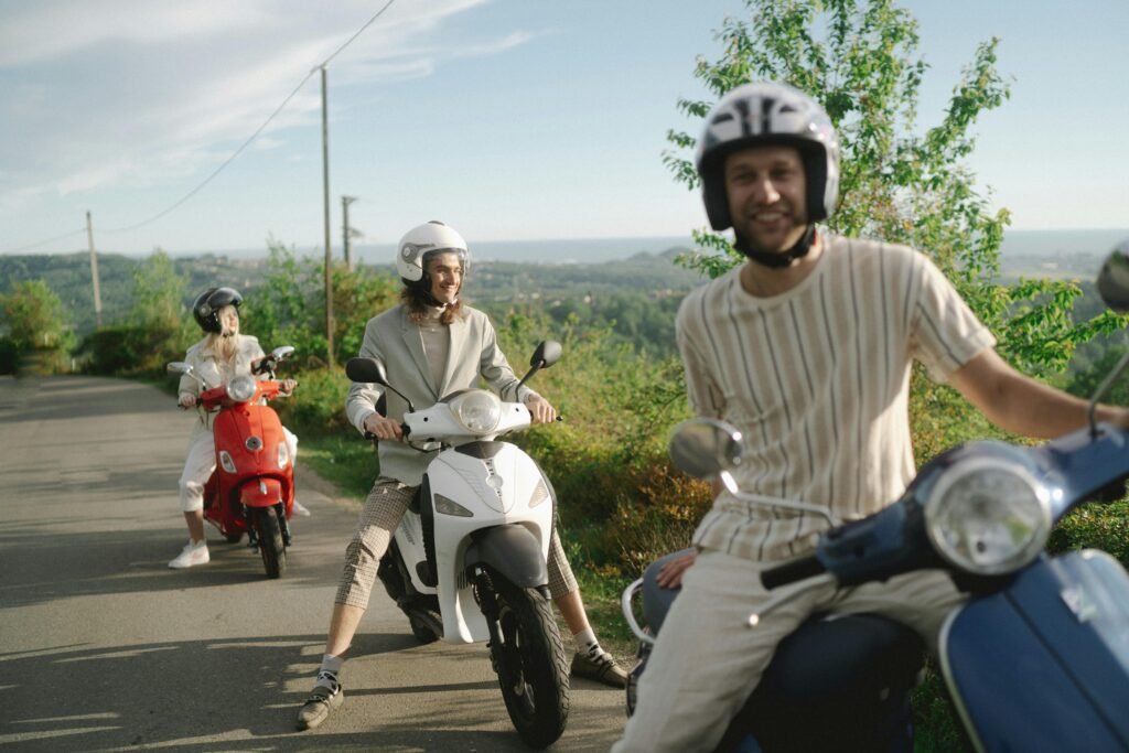 Three friends on scooters enjoy a scenic road ride in a lush landscape, embodying freedom and adventure.